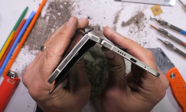 Hands holding a damaged foldable smartphone, showing a bent hinge and cracked screen.