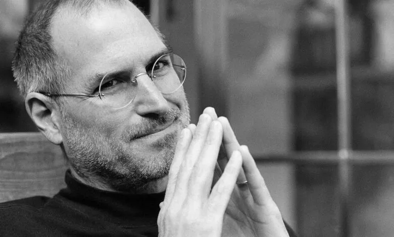 Close-up black and white portrait of Steve Jobs with his hands clasped.