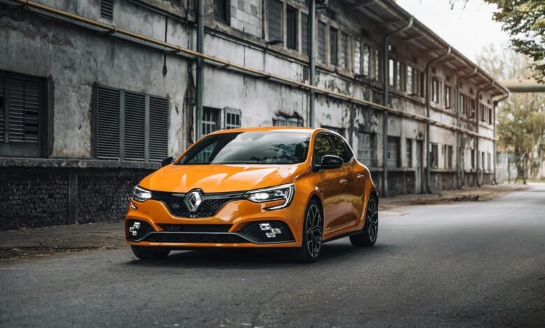 Orange Renault Megane RS parked on an asphalt road in front of an old industrial building.