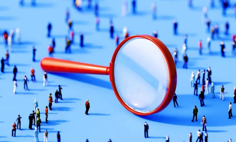 A large red magnifying glass hovers over a crowd of tiny, blurred figures on a blue background.