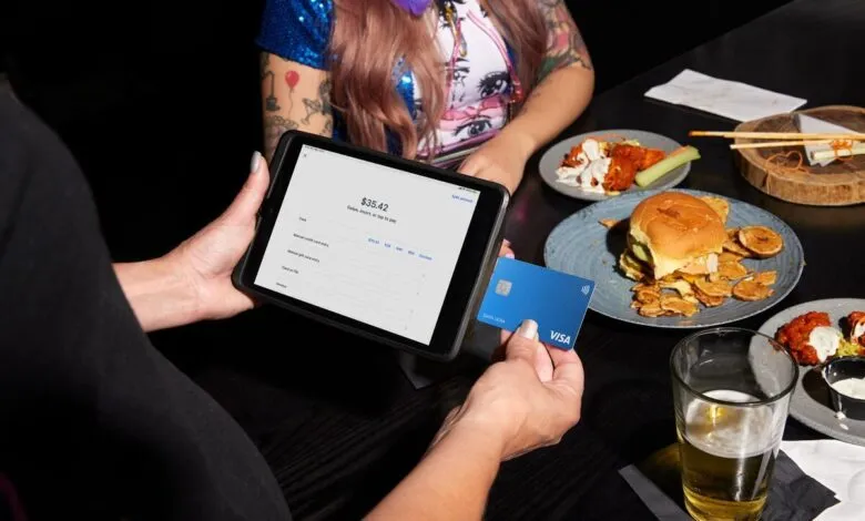 Person paying with a Visa card on a tablet at a restaurant table with food.