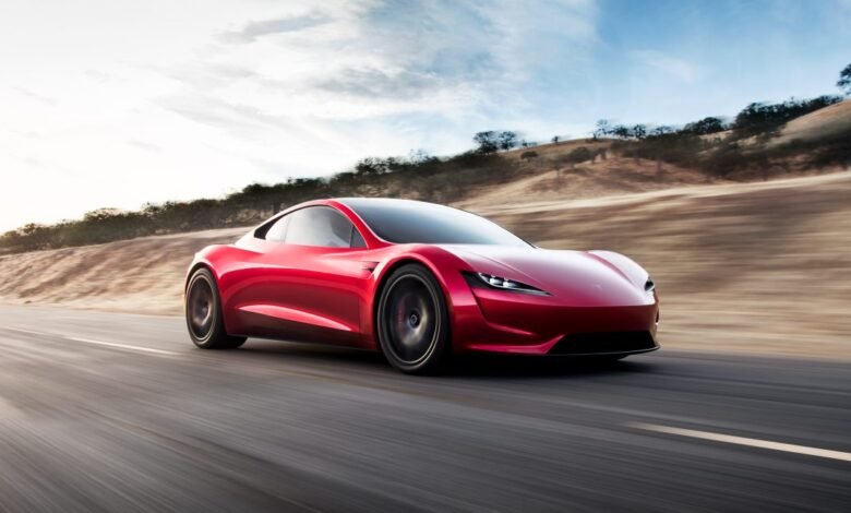 A sleek red Tesla Roadster drives on a highway with a blurred background.