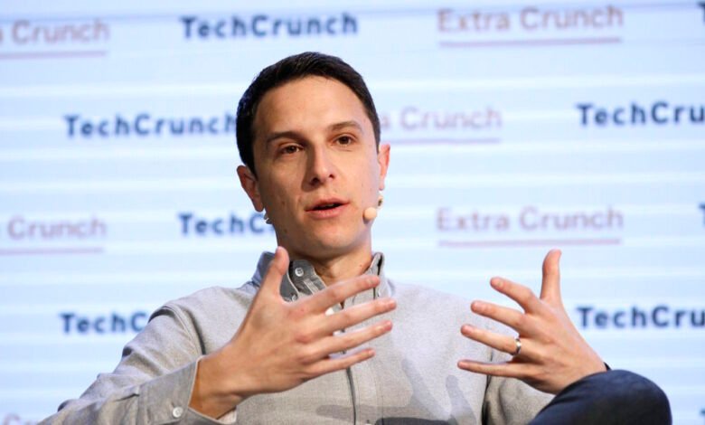 Man speaking with hands gesturing, wearing a light grey shirt and microphone.