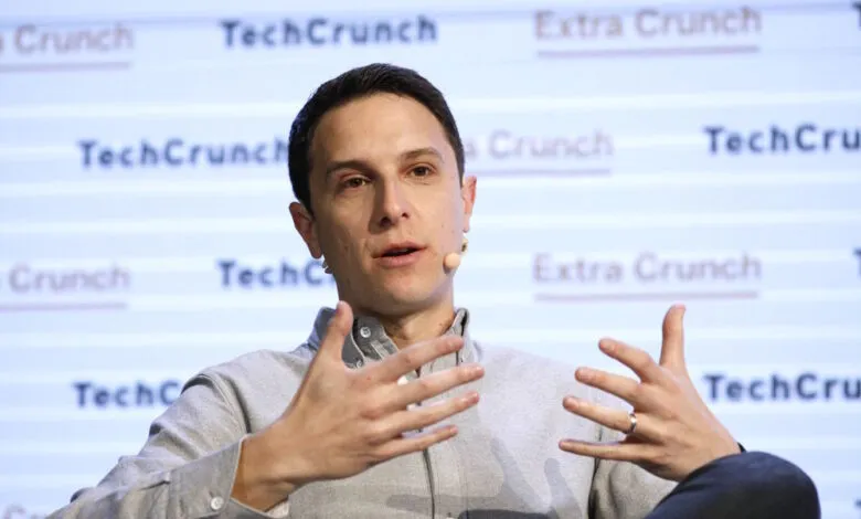 Man speaking with hands gesturing, wearing a light grey shirt and microphone.