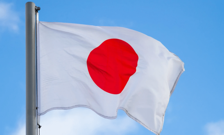 The flag of Japan, a white rectangle with a large red disc in the center, waves against a bright blue sky.