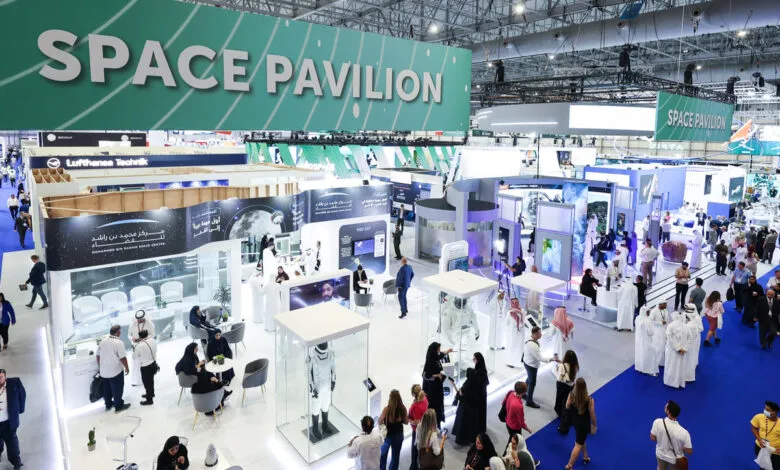 Busy exhibition hall with a large 'SPACE PAVILION' banner overhead, featuring various booths and attendees.