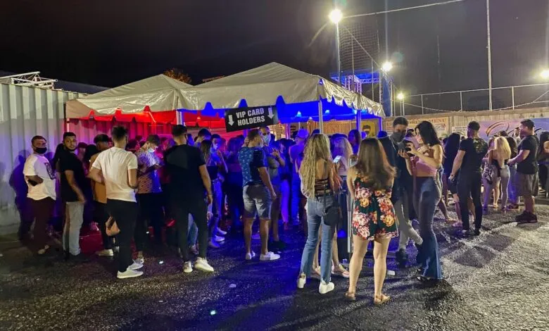 Crowd of people gathered outside tents at night, with red and blue lighting.
