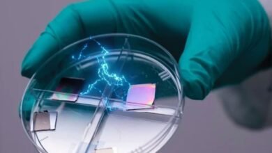 Gloved hand holding petri dish with iridescent squares and blue electrical sparks.