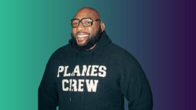 A smiling Black man with glasses and a beard wears a dark hoodie with 'PLANES CREW' on it.