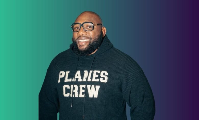 A smiling Black man with glasses and a beard wears a dark hoodie with 'PLANES CREW' on it.