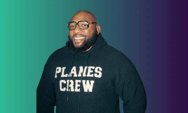 A smiling Black man with glasses and a beard wears a dark hoodie with 'PLANES CREW' on it.
