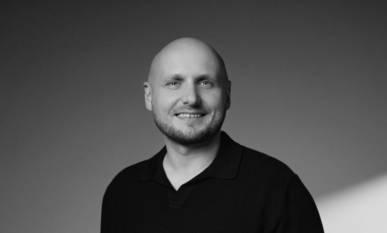 Bald man with a beard and a black collared shirt smiles at the camera.