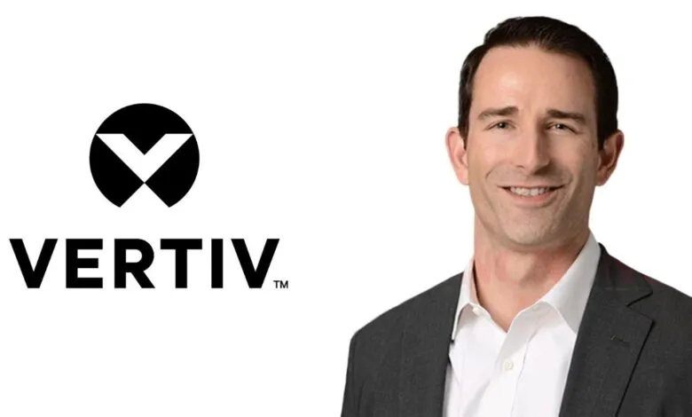 Man in suit smiling next to Vertiv logo