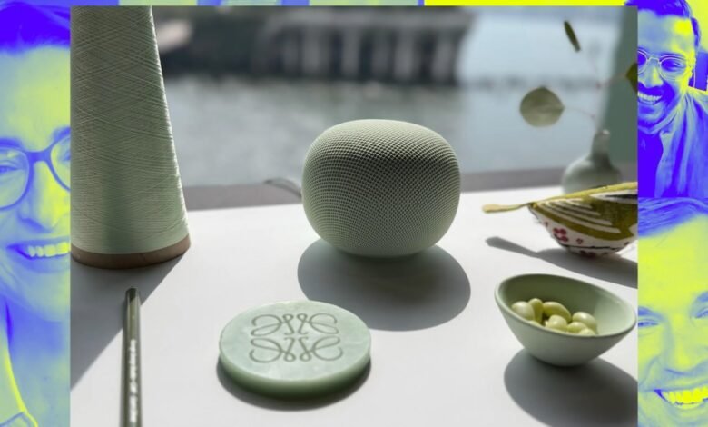 A light green smart speaker sits on a white surface next to a spool of thread and a decorative item.