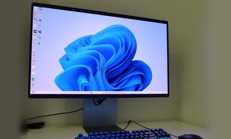 A modern computer monitor displaying the Windows 11 logo and a keyboard with blue backlighting.