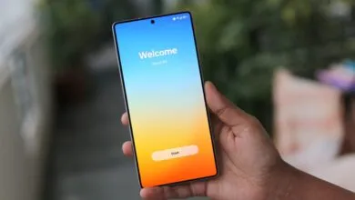 Hand holding a smartphone displaying the One UI 8.5 welcome screen with a 'Start' button.