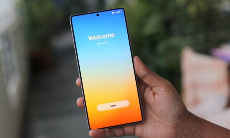 Hand holding a smartphone displaying the One UI 8.5 welcome screen with a 'Start' button.