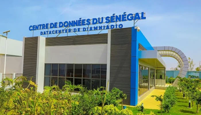 Modern datacentre building with blue signage and lush green landscaping.