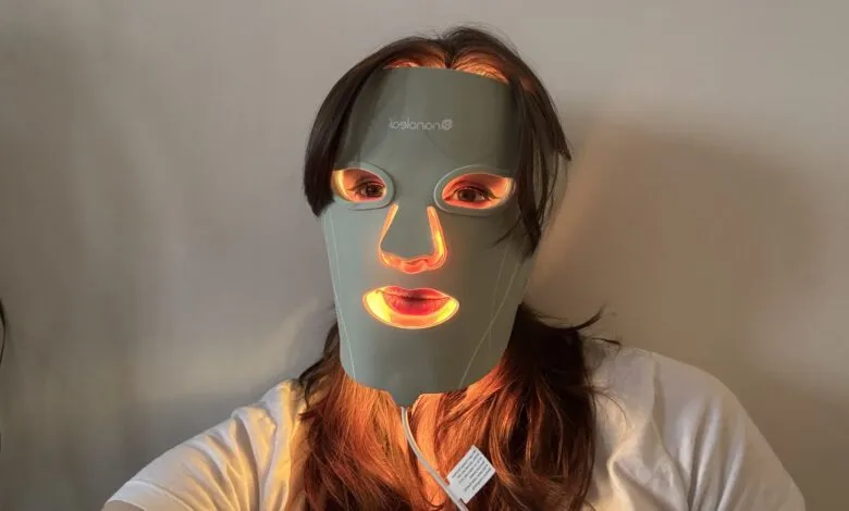 Woman wearing a light therapy mask with orange and red LEDs illuminating her face.