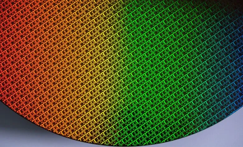 Close-up of a silicon wafer with intricate patterns and a rainbow gradient.