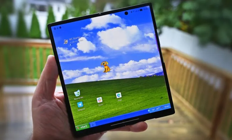 Hand holding a foldable smartphone displaying Windows XP desktop wallpaper.