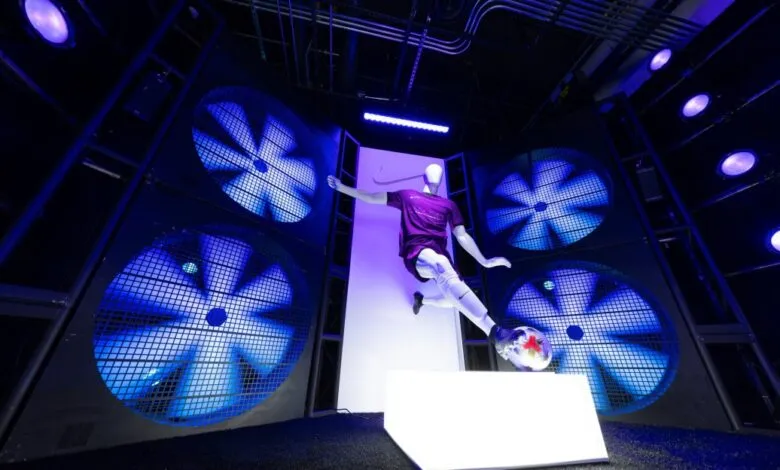 Mannequin in soccer gear mid-air, kicking a ball, with large blue fans behind.
