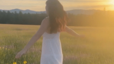 Woman in white dress twirling in a sun-drenched field with mountains in the background.