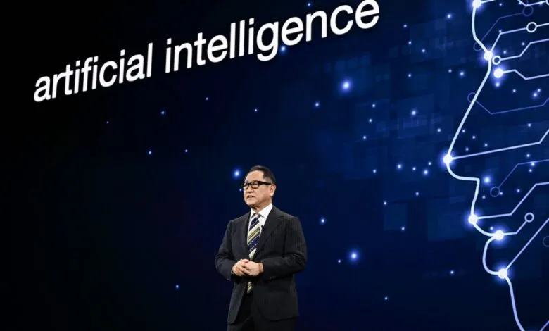 Akio Toyoda speaks on stage with 'artificial intelligence' displayed behind him.