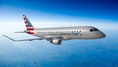An American Eagle regional jet flies through a clear blue sky over a landscape.