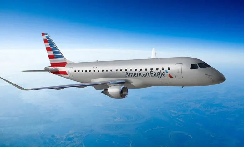 An American Eagle regional jet flies through a clear blue sky over a landscape.