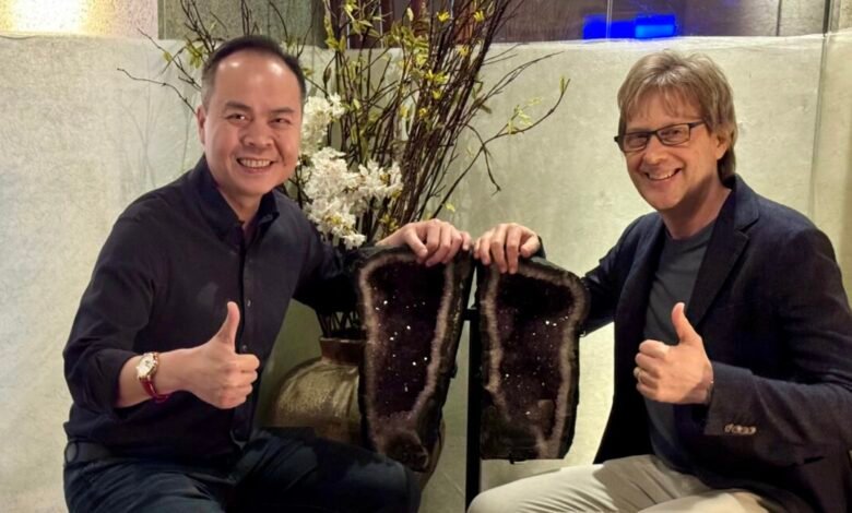 Two men holding a large split amethyst geode, giving thumbs up.
