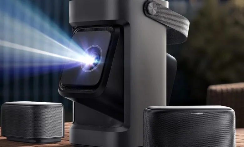 Portable projector with speakers projecting a blue light beam outdoors.