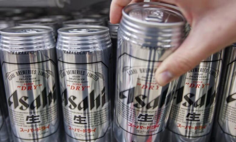 A hand reaches for a can of Asahi Super Dry beer from a row of cans.