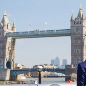Man in a blue suit standing with Tower Bridge in London behind him.