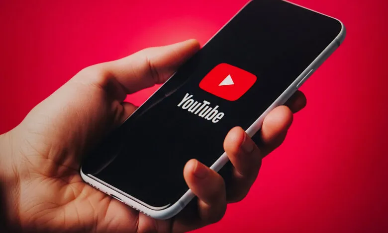 Close-up of a hand holding a smartphone displaying the YouTube logo.