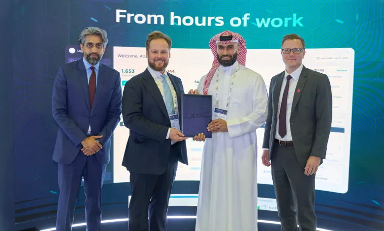 Four men in business attire stand in front of a large screen displaying data.