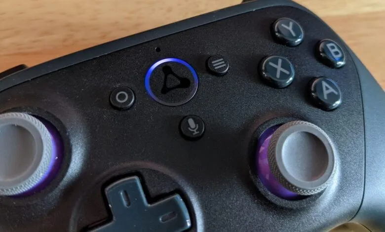 Close-up of a black gaming controller with illuminated buttons and analog sticks.