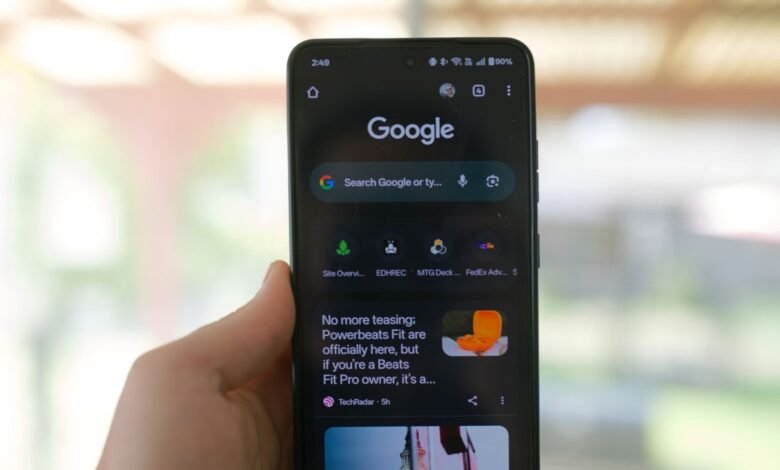 A hand holds a smartphone displaying the Google search engine homepage in dark mode.