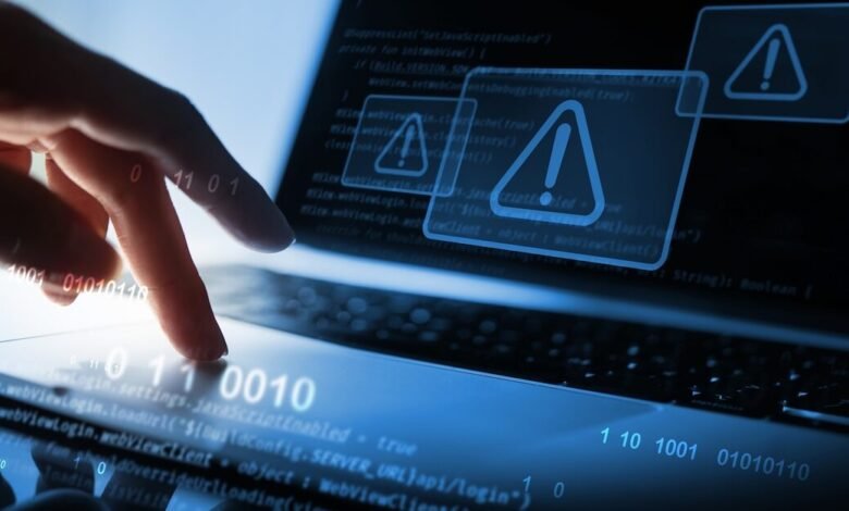 Close-up of a hand interacting with a laptop displaying code and warning symbols.