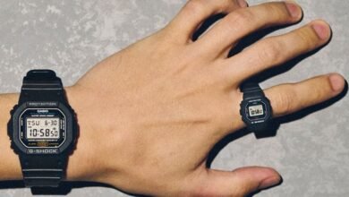 A person's hand wearing a Casio G-Shock watch on the wrist and a miniature G-Shock watch as a ring.