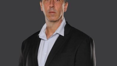 Portrait of a man in a suit and light blue shirt against a dark gray background.