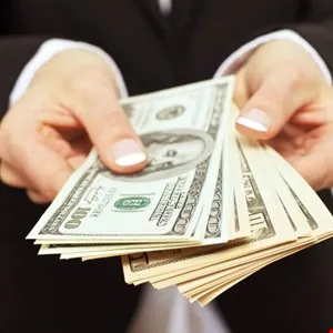 Hands holding a fan of US dollar bills, including $100 and $10 denominations.
