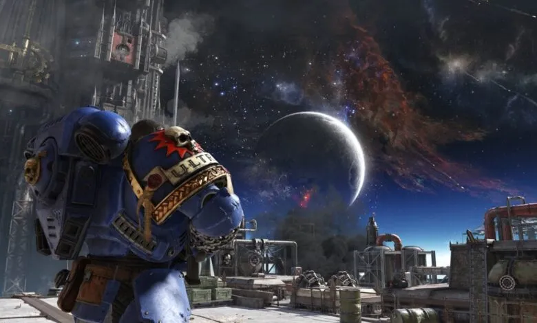 A blue space marine in power armor stands on a platform overlooking a futuristic industrial landscape under a starry sky with a large moon.