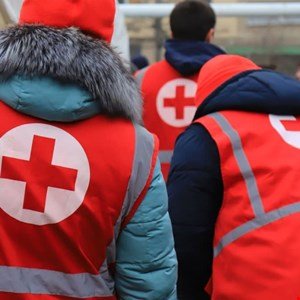 Volunteers in red vests with white Red Cross emblems, seen from behind.