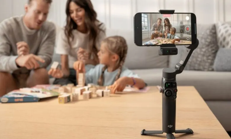 Family playing a board game while being filmed by a smartphone on a gimbal.