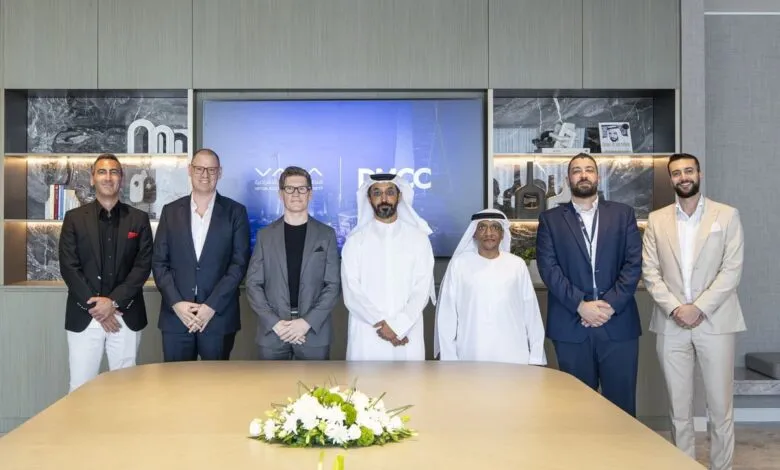 Seven men in business attire and traditional Emirati dress stand behind a conference table.