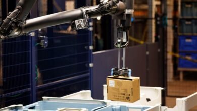 Robotic arm picking up a cardboard box in a warehouse setting.