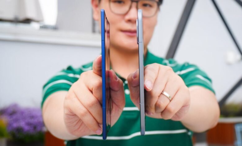 Person holding two smartphones side-by-side, one blue and one silver, for comparison.