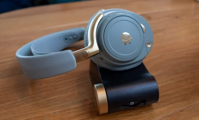 Close-up of a gray SteelSeries headset with gold accents on a charging stand.