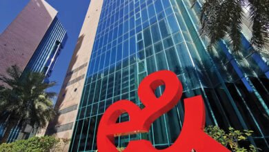 Large red 'e&' logo in front of modern glass skyscrapers under a clear blue sky.